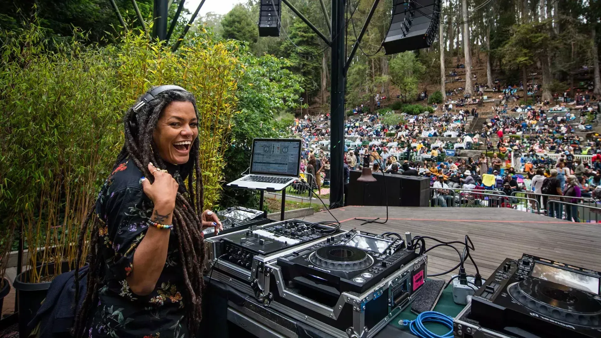 Uma mulher discotecando no Stern Grove Festival olha por cima do ombro e sorri para a câmera.