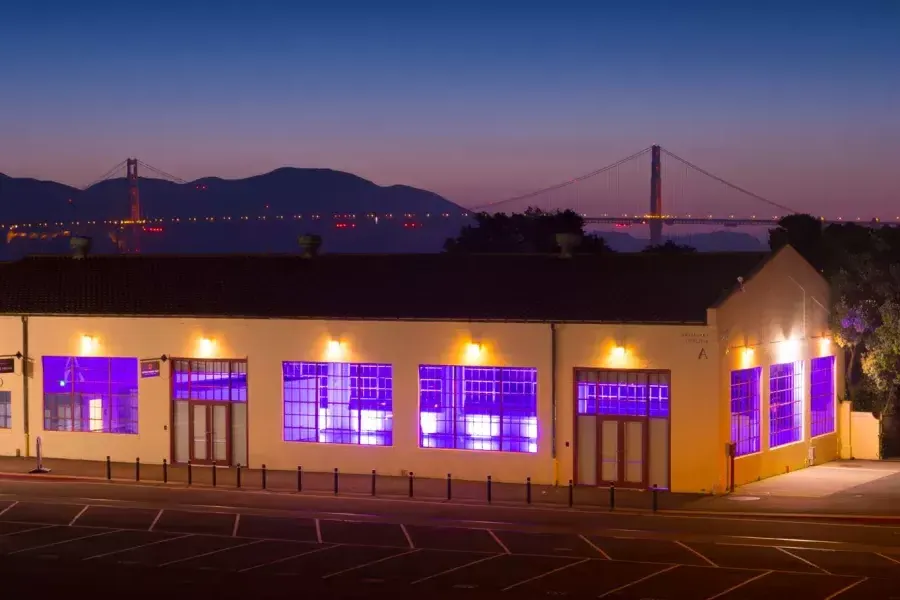 Fort Mason 건물은 밤에 다리를 배경으로 보라색 실내 조명으로 밝혀집니다.