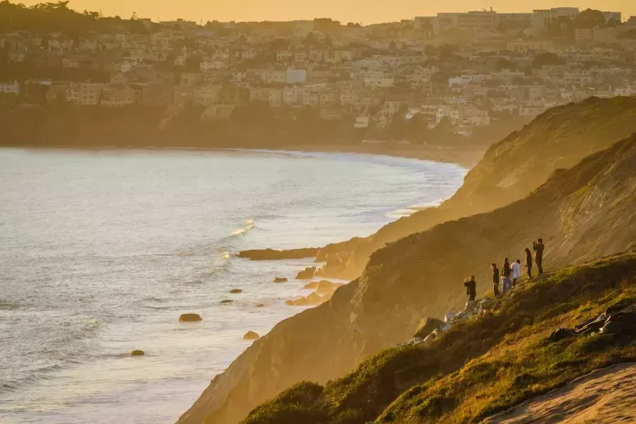 Un grupo de personas se encuentra en un acantilado frente al mar contemplando la puesta de sol en el Presidio de San Francisco.