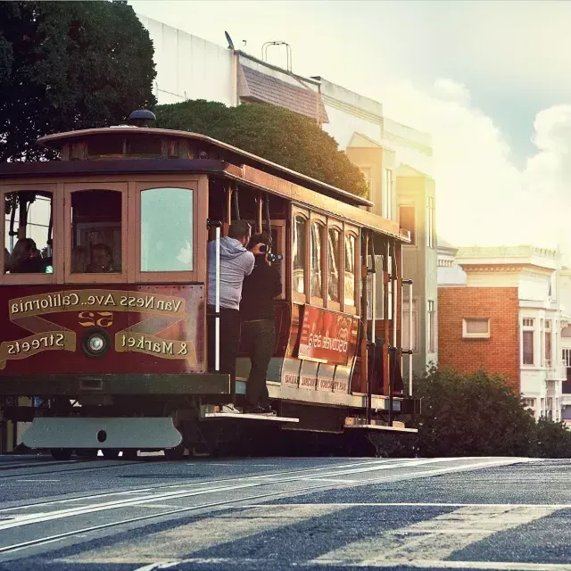 Eine Seilbahn fährt um einen Hügel in San Francisco, während die Passagiere aus dem Fenster schauen.