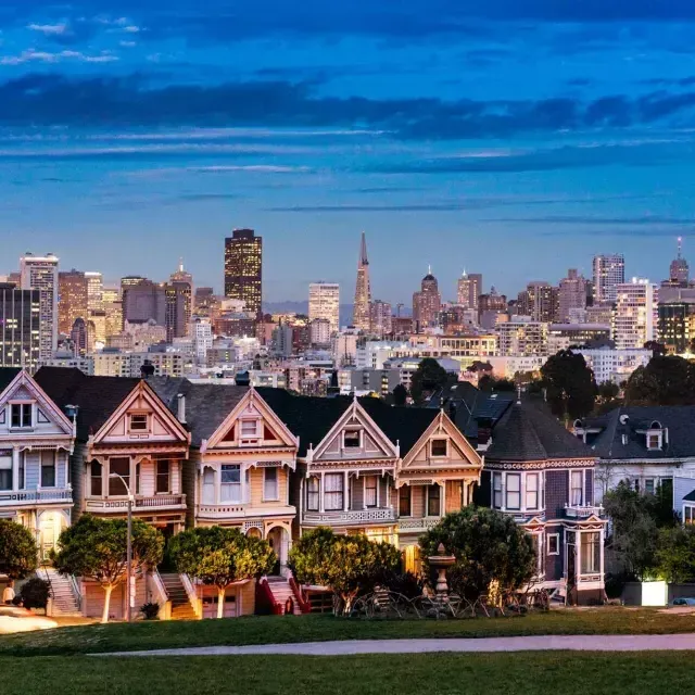 Die berühmten Painted Ladies vom Alamo Square sind in der Dämmerung vor der Skyline von San Francisco zu sehen.