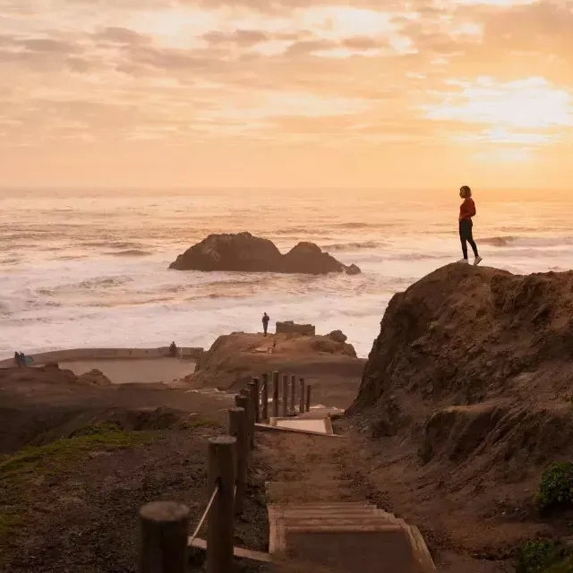 Duas pessoas estão em cima de pedras com vista para o oceano em Sutro Baths, em São Francisco.